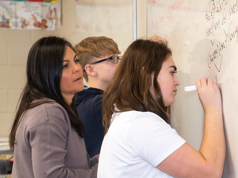 Teacher helping math students at the white board